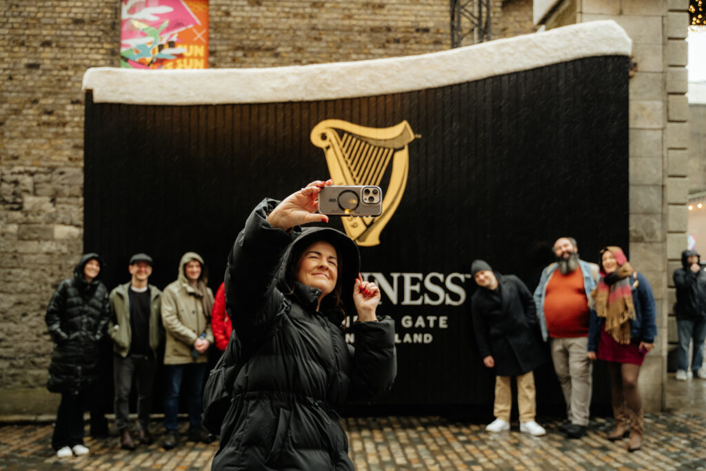 A guide stands and poses for a photo with her groups of guests in front of the famous Guinness factoy gates