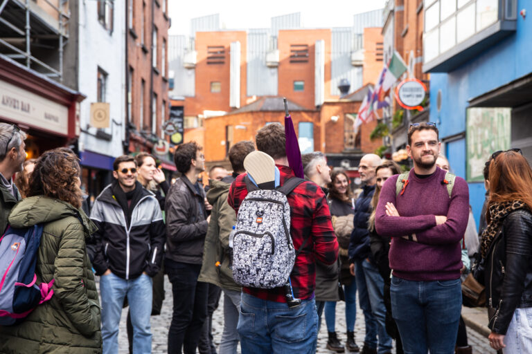 A tour guide standing in the temple bar neighbourhood guiding a group of tourists holding a purple umbrella