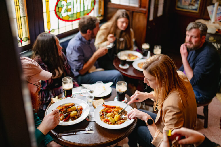 A group of people sat around a table in a snug in an irish pub in dublin enjoying local irish food as they receive a tour on what they're eating