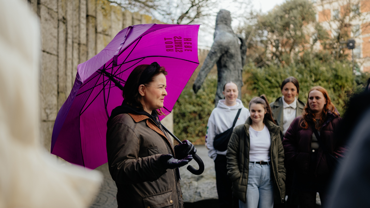 A tour guide with unearthed tours, guiding a group on the discover dublin & hidden gems free tour, holding a purple umbrella
